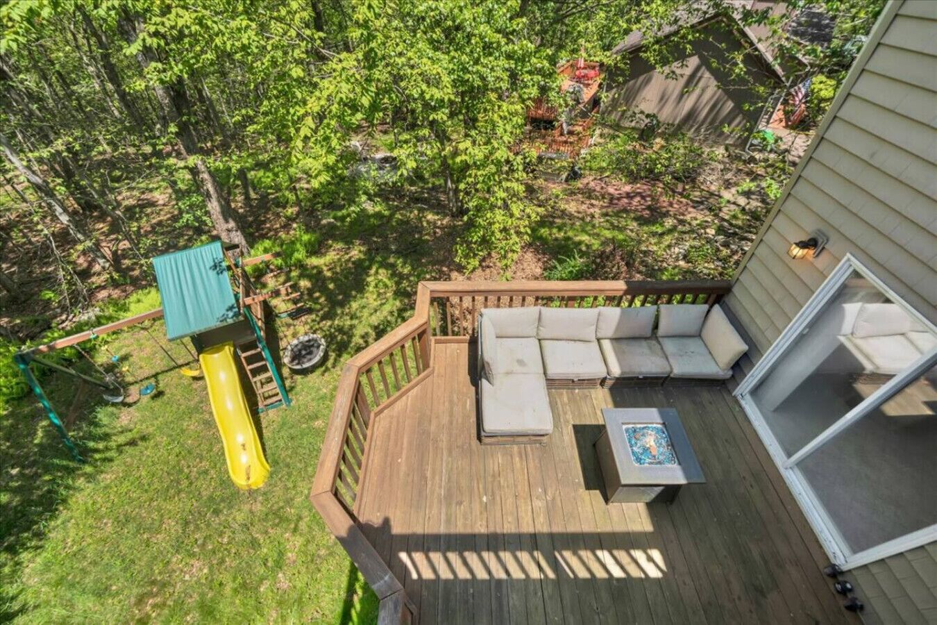 A wooden deck with a built-in sofa and a small table, surrounded by a wooden railing and a slide.