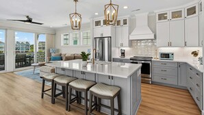 A modern kitchen with a large island, stainless steel appliances, and a view to the outside. - The Pointe of No Return (Ocean Isle Beach)