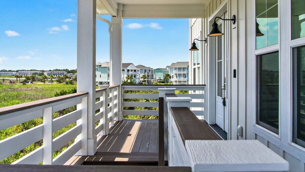 A covered porch with a wooden deck, white railings, and a view of a residential area. - The Pointe of No Return (Ocean Isle Beach)