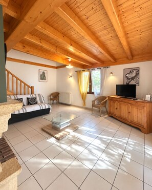 A spacious living area with a wooden ceiling, a sofa, a glass coffee table, a TV, and a cabinet.
