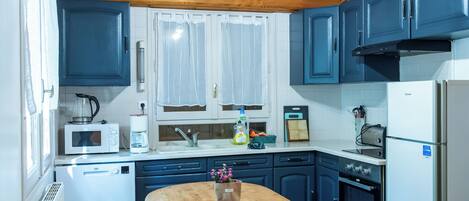 A kitchen with wooden beams, a central island with benches, white cabinets, and a refrigerator.