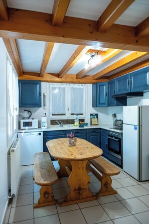 Una cocina con vigas de madera, una isla central con bancos, armarios blancos y un refrigerador.