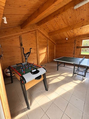Una habitación con mesa de fútbolín, mesa de ping pong y ventana que deja entrar luz natural.