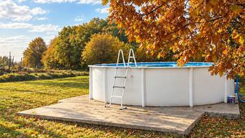 Une piscine extérieure avec un escalier, entourée de gazon et de feuilles d’automne.