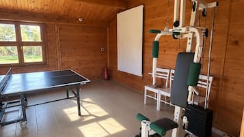 Une salle de sport équipée de matériel d’exercice, d’une table de ping-pong et d’une fenêtre donnant sur un espace verdoyant.