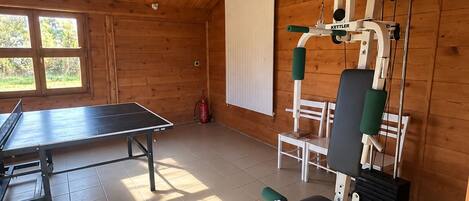 Un gimnasio con equipo de ejercicio, mesa de ping pong y ventana con vista a zonas verdes.