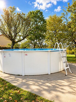 A round swimming pool with a ladder, surrounded by trees and a clear sky.