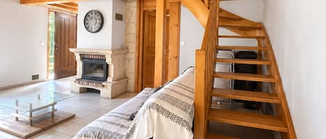 A spacious room with a wooden staircase leading to an upper level, a fireplace, and a bed with a blanket.