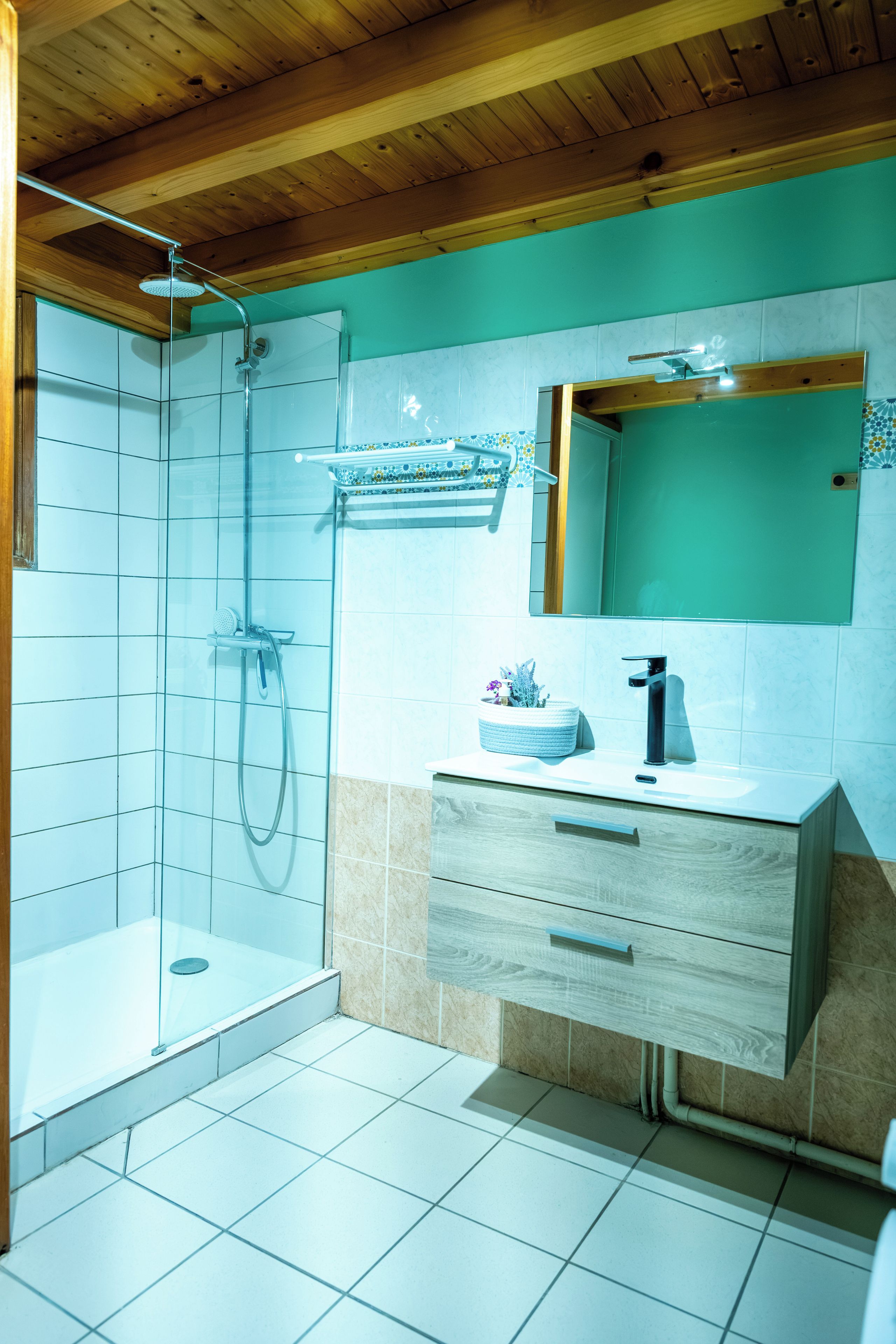 Een badkamer met een douchecabine van glas, een wastafel met spiegel erboven en een betegelde vloer.