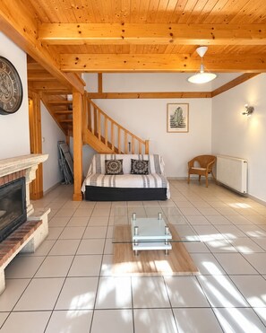 Una sala de estar moderna con una escalera de madera, un sofá con cojines estampados, una mesa de centro de vidrio y una chimenea.