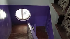 Portaat, joissa on puiset askelmat ja violetti kaide, johtavat ylätasanteelle, jossa on pyöreä ikkuna.