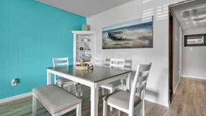 Un comedor con una mesa y sillas blancas, una pared de acento color turquesa y un cuadro de un barco en la pared.