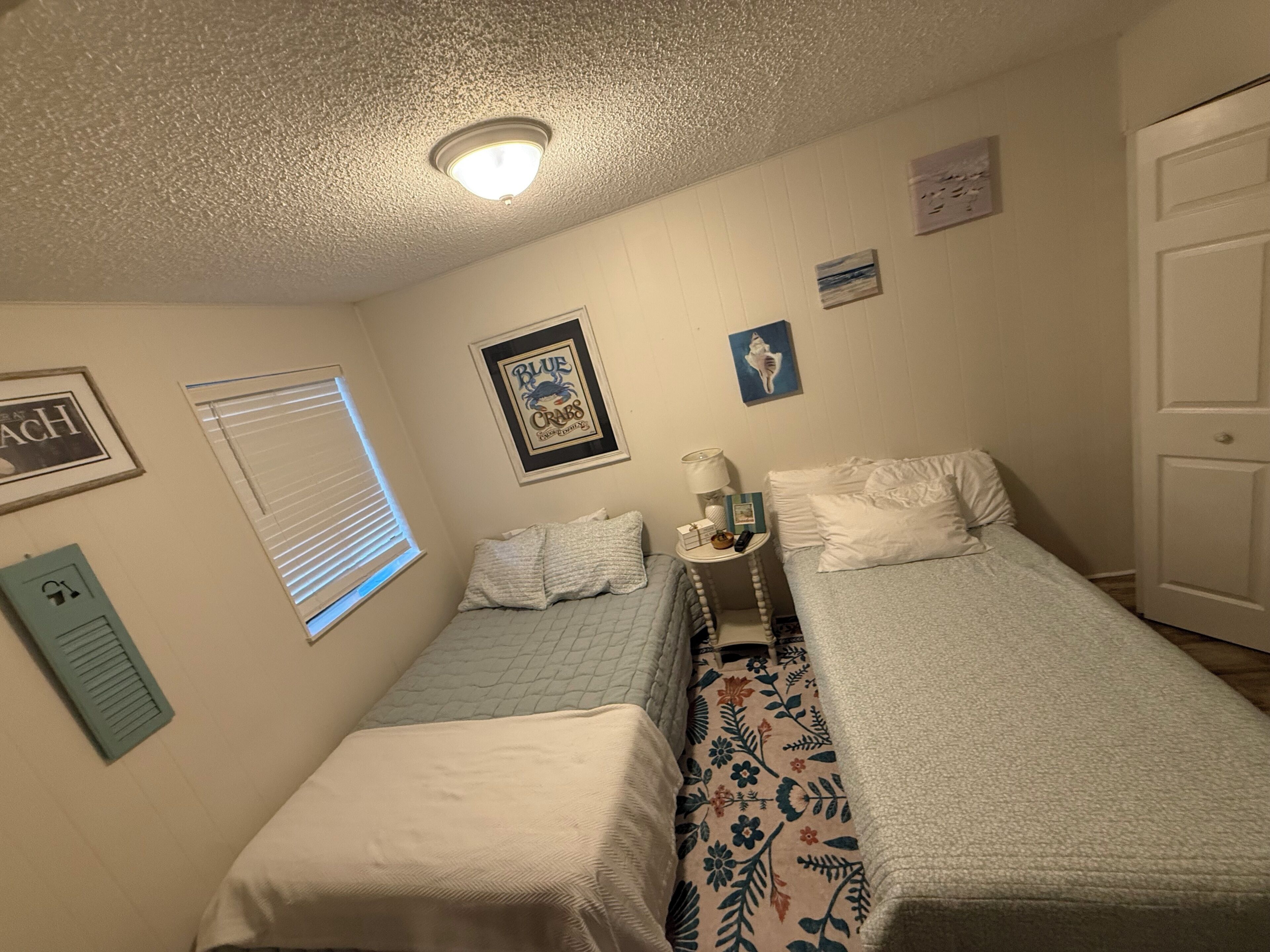 A bedroom with two beds, a window with blinds, a ceiling light, and wall decorations.