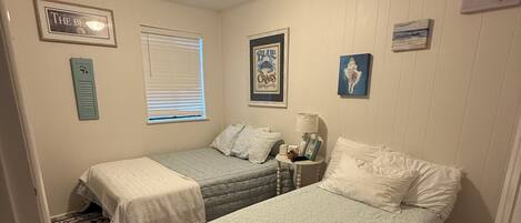 A bedroom with two beds, a window, a ceiling light, and a floral-patterned rug.