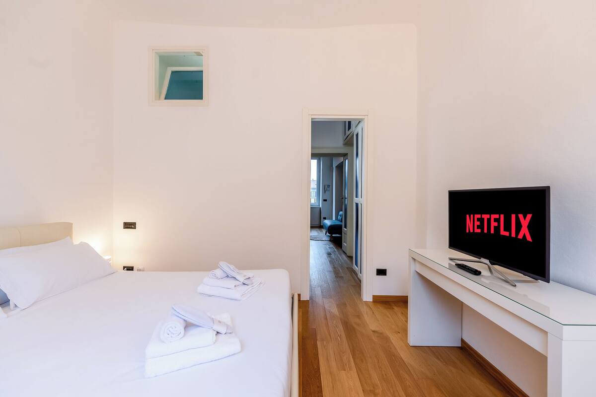 A hotel room with a bed, a TV displaying 'NETFLIX', and a glass desk.