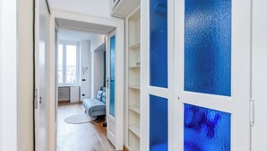 A hallway with a light wooden floor, a grey sofa, and a white door with blue glass panels. - Bramante Luxury Apartments by InnStay (Milan)