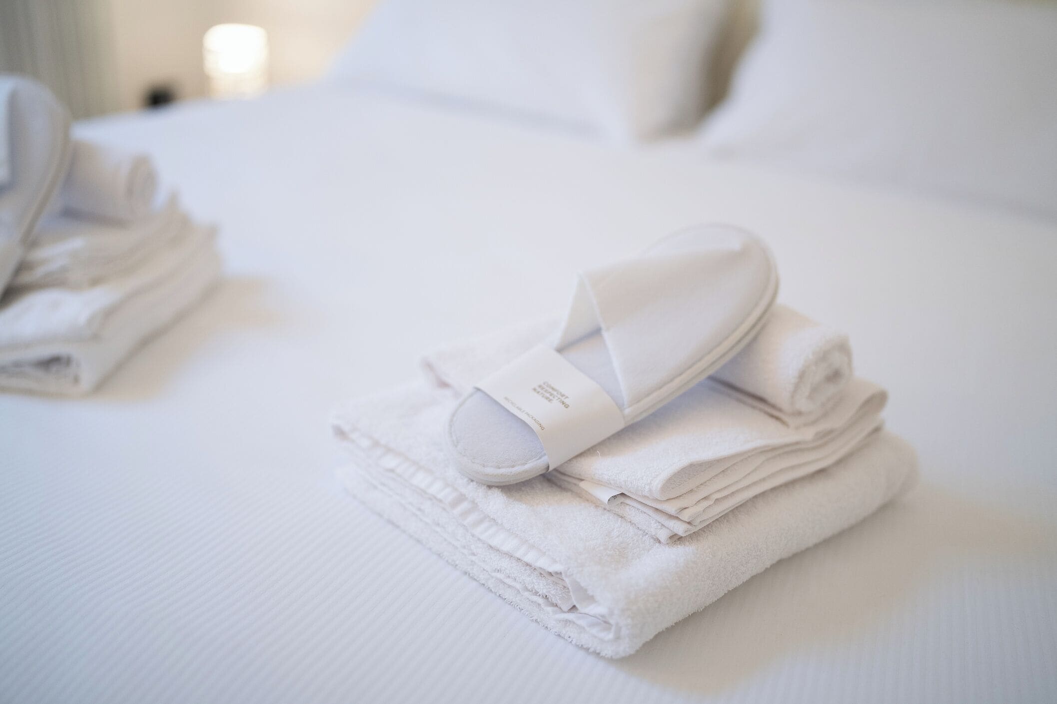 Une pile de serviettes blanches soigneusement pliées et un appareil de massage électrique blanc sont posés sur un lit recouvert de draps blancs.