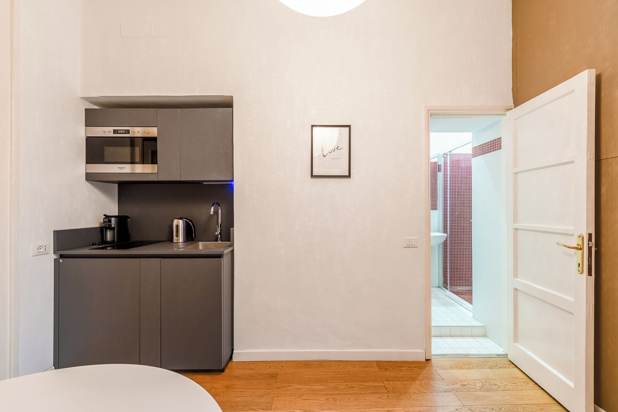 A compact kitchen with modern appliances, a framed inspirational quote on the wall, and a wooden floor.