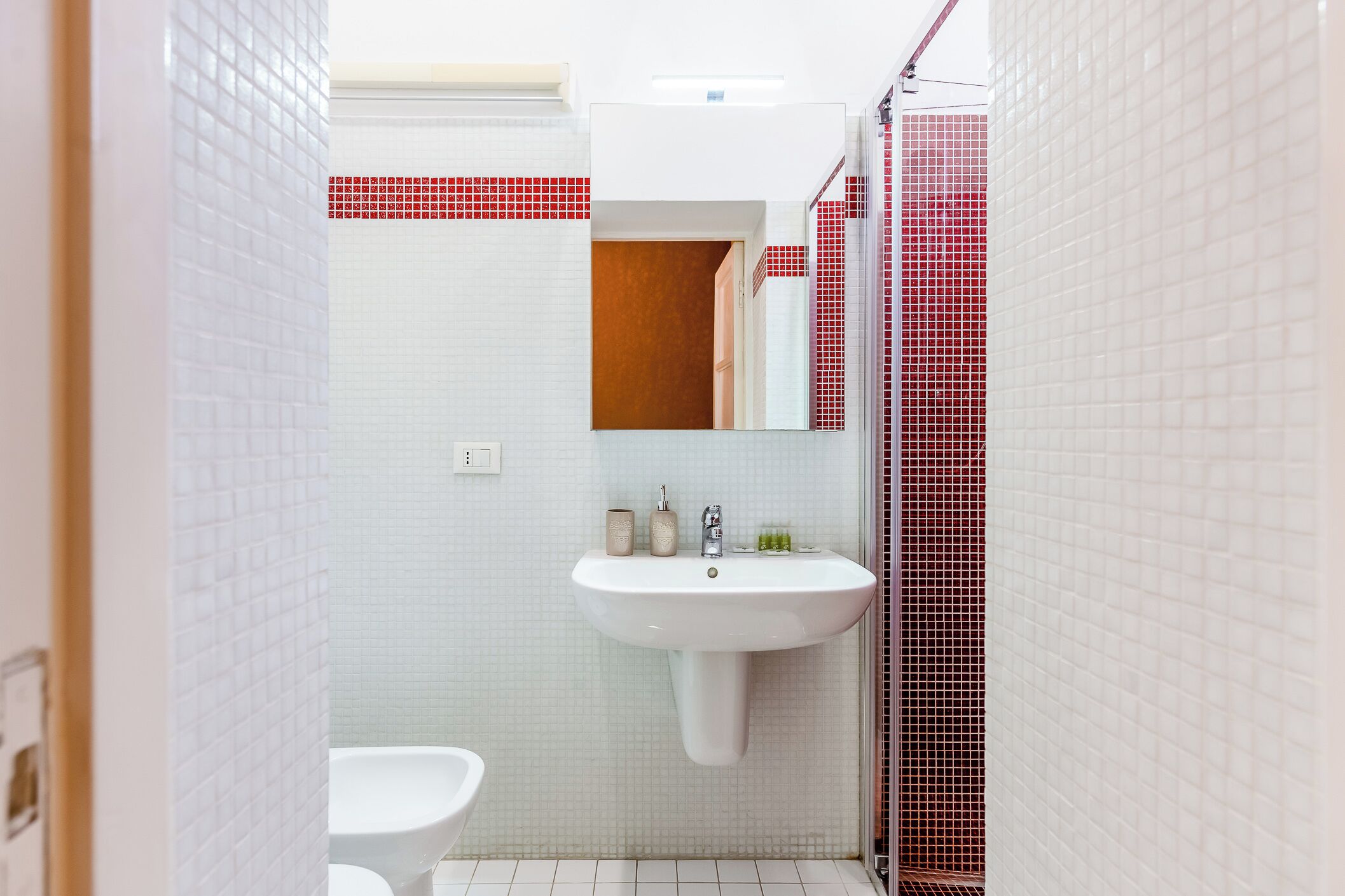 A bathroom with a white sink, a mirror, and red-tiled shower area.