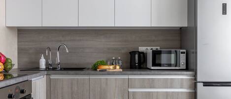 A modern kitchen with grey cabinets, a stainless steel refrigerator, a microwave, and a sink.