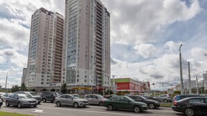 Un edificio de varios pisos con numerosas ventanas y balcones, rodeado de coches estacionados y un cielo despejado con nubes.