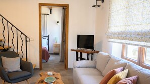 Una sala de estar con sofá, sillón, mesa de centro de madera y televisor.