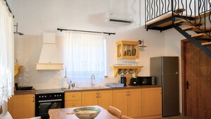 Cocina compacta con comedor, armarios de madera, horno empotrado y refrigerador de acero inoxidable.