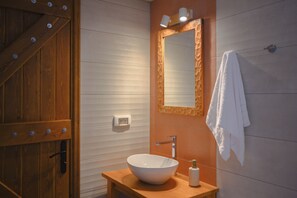 A bathroom with a wooden door, a white sink with a vessel basin, a mirror with a decorative frame, and a towel hanging on the wall.