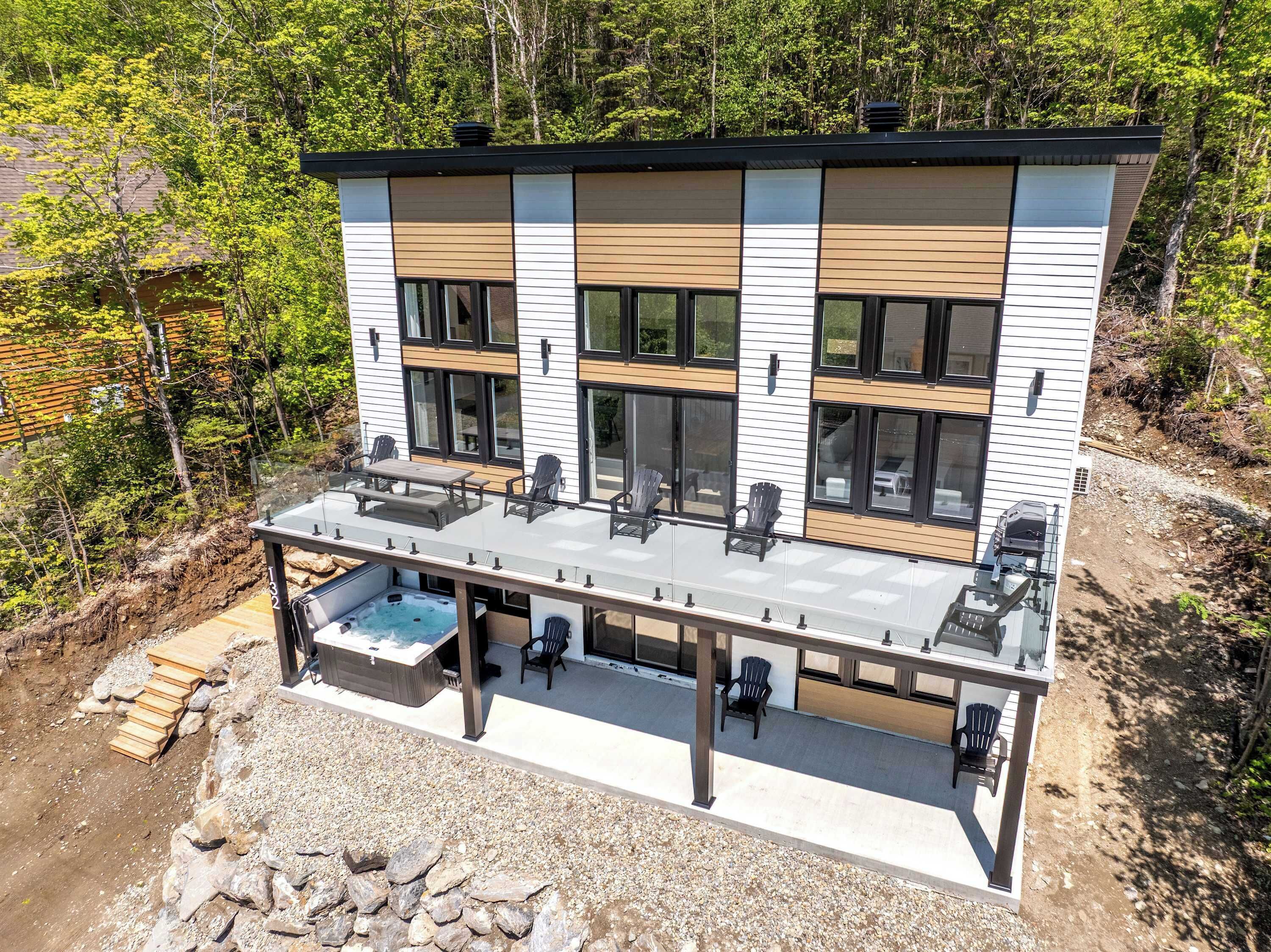 Et moderne hus med to etager, en terrasse, udendørs møbler og et spabad.