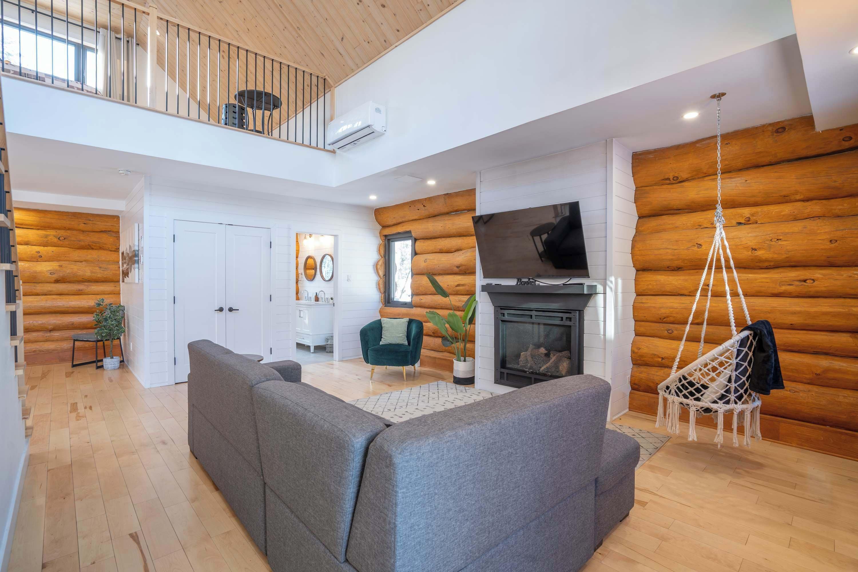 A spacious living area with a grey sofa, a hanging chair, and a fireplace.