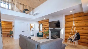 A spacious living area with a grey sofa, a hanging chair, and a fireplace. - Spa & Pool table | Le Massif (Saint-Adolphe-d'Howard)