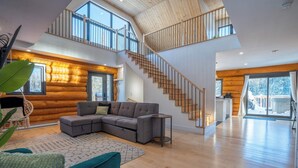 A spacious living area with a large sectional sofa, a staircase, and a view of the outdoors. - Spa & Pool table | Le Massif (Saint-Adolphe-d'Howard)