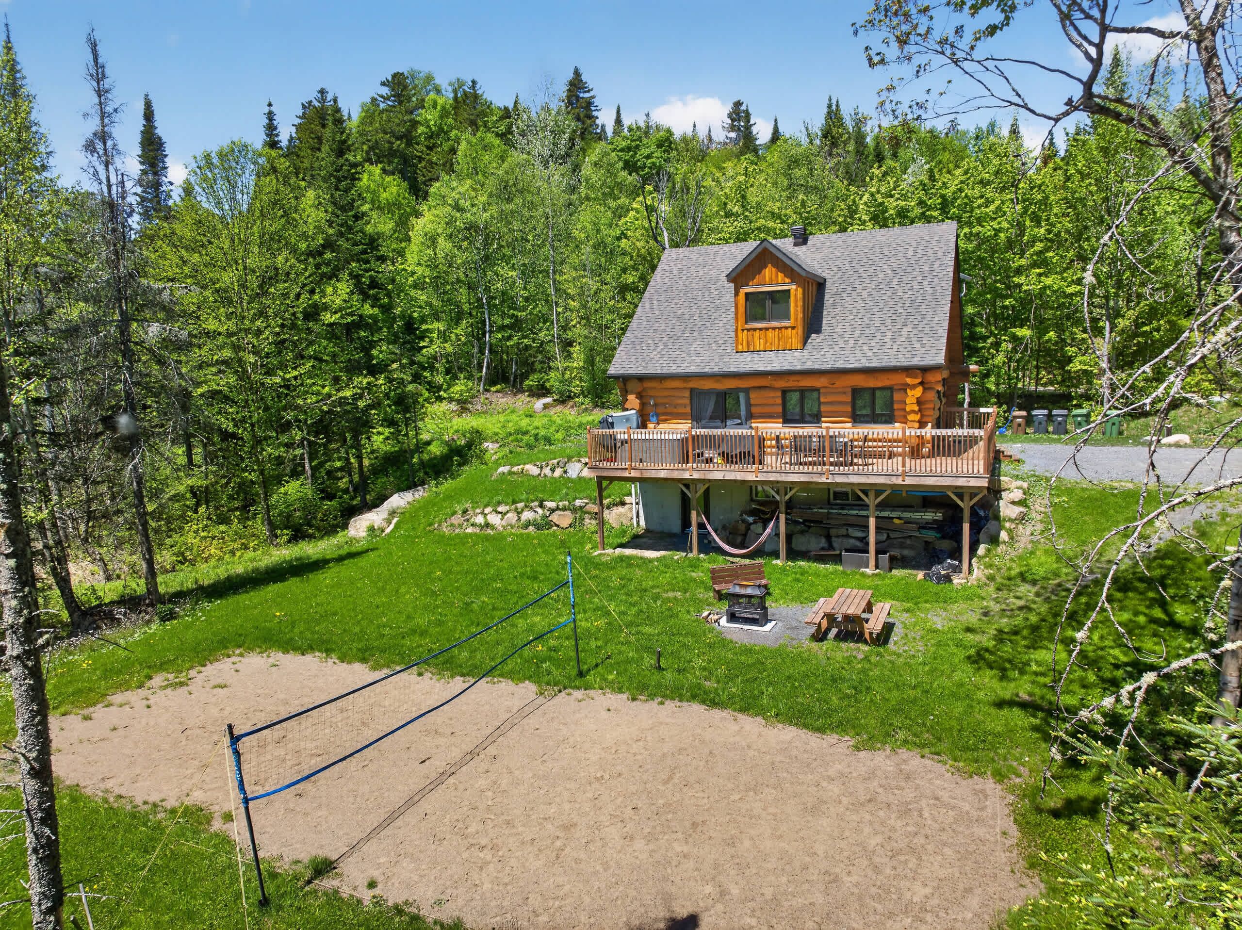 A log cabin with a deck, surrounded by a grassy yard and trees.