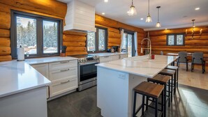 A modern kitchen with wooden walls, a central island, and a dining area with bar stools. - Spa & Pool table | Le Massif (Saint-Adolphe-d'Howard)