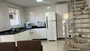 A modern kitchen with white cabinets, a stainless steel refrigerator, and a black countertop. There is a dining area with a glass table and brown chairs. A staircase with metal railings leads to another level. - Center of Brasilia 5 minutes from the Esplanade of Ministries (Brasília)