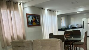 A living room with a beige sofa, a dining table with chairs, and a kitchen in the background. - Center of Brasilia 5 minutes from the Esplanade of Ministries (Brasília)