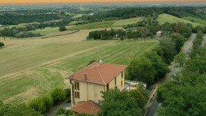 Una casa con techo de tejas rojas, rodeada de campos verdes y árboles.