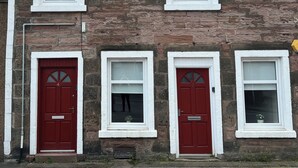 A row of three red doors with white-framed windows on a stone building. - 2 Lower Kessock Street (Inverness)