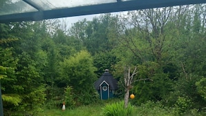 Een klein, blauw gebouw met een donker dak, omgeven door weelderige begroeiing en een verhard gebied op de voorgrond.