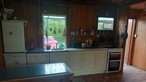 Een keuken met houten kastjes, een koelkast, een spoelbak, een fornuis en een raam met uitzicht op een rode auto erbuiten.