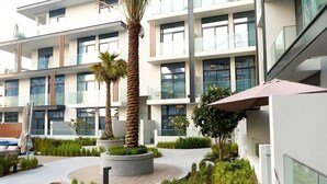 Een modern gebouw met meerdere verdiepingen, grote ramen en een aangelegde binnentuin met palmbomen en planten.