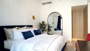 Een moderne slaapkamer met een groot bed, een spiegel, een plant en een houten deur.