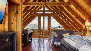 Un dormitorio acogedor en el ático con techo de madera, una cama, un escritorio y vistas a las montañas.