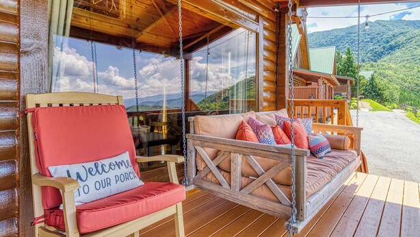 Un porche de madera con una mecedora y una silla acolchada, ambos con cojines, con vistas a un paisaje montañoso.