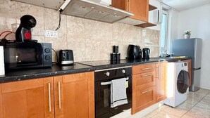 A modern kitchen with wooden cabinets, a built-in oven, a microwave, a coffee maker, and a washing machine.