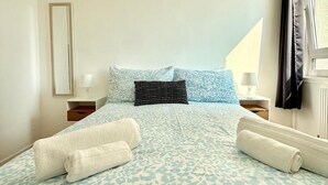 A bedroom with a bed, pillows, a nightstand, a lamp, and a window with curtains.