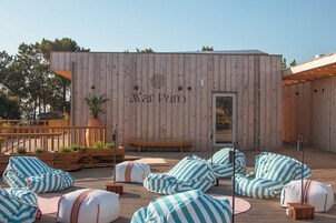 Un edificio de madera con un letrero que dice 'Mar Puro' y un área de terraza con sillones de mimbre y un banco.