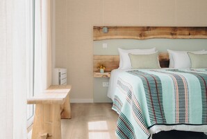 Un dormitorio con cabecera de madera, una mesita de noche con un florero y una cama con manta a rayas.