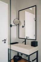 Un baño moderno con un lavamanos blanco, un grifo negro y un espejo redondo con marco negro.
