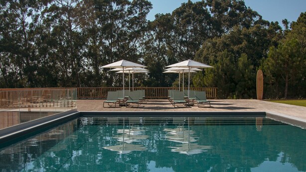 A swimming pool with lounge chairs and umbrellas, surrounded by trees. - Mar Puro (Mafra)